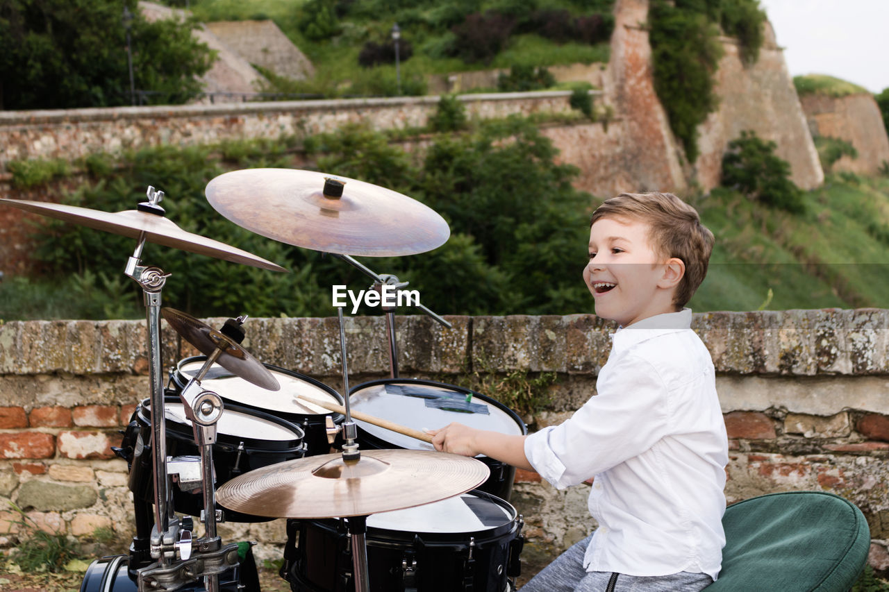 Smiling boy playing drum kit outdoors