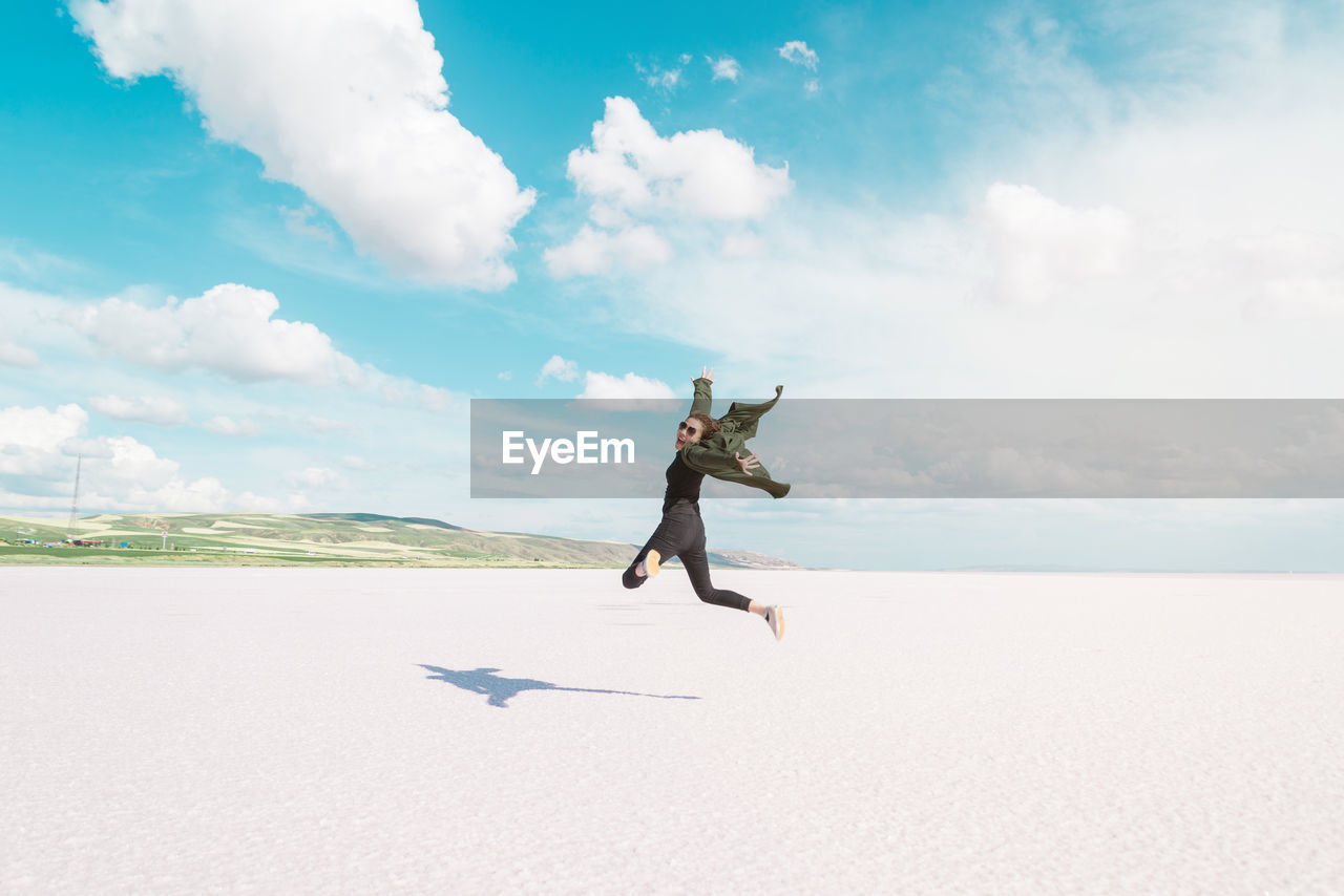 Full length rear view of woman jumping at beach during sunny day