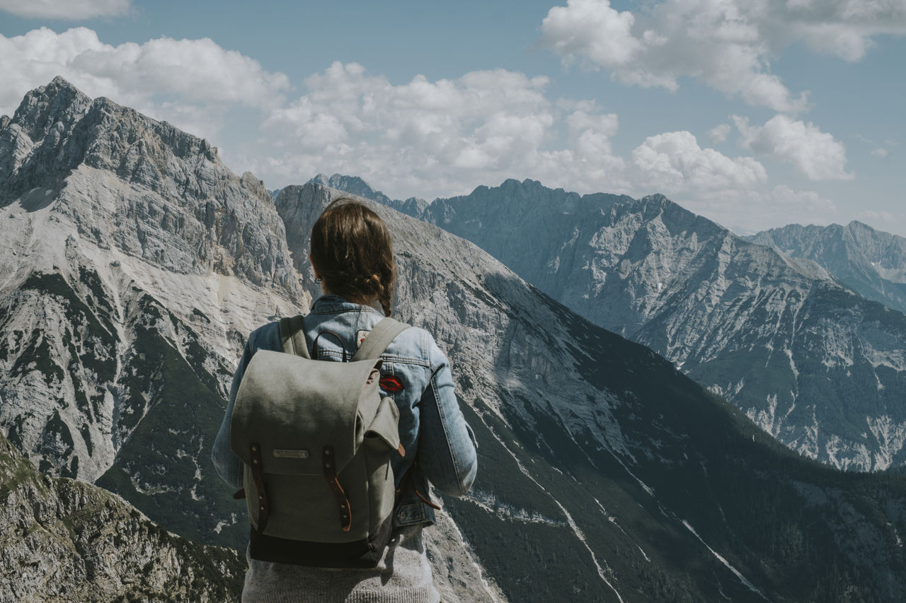 Rear view of woman with backpack looking at mountains against sky