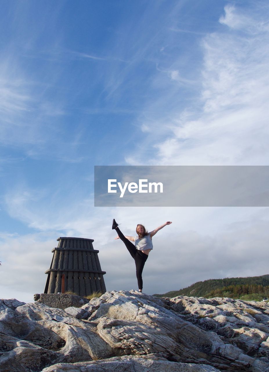 Full length of teenage girl practicing yoga on rocks against sky