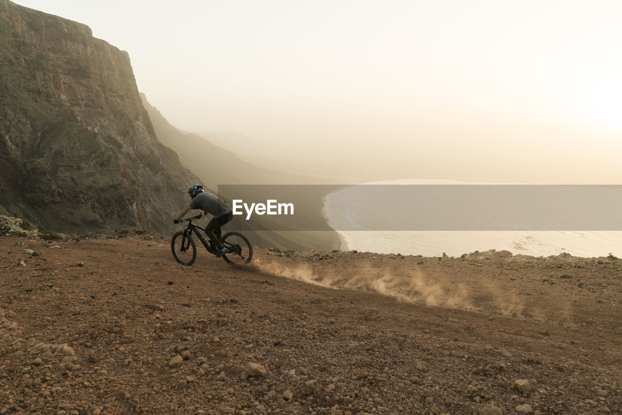 Spain, lanzarote, mountainbiker on a trip at the coast at sunset
