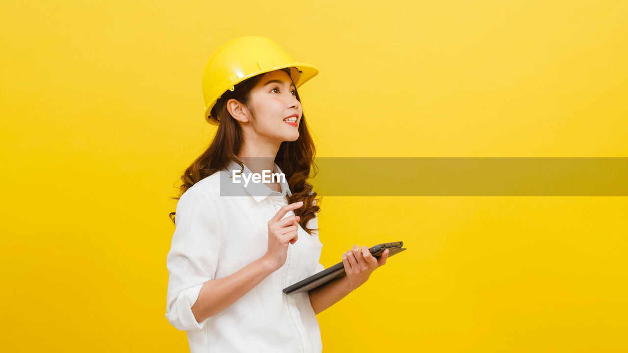Smiling female architect holding digital tablet against yellow background