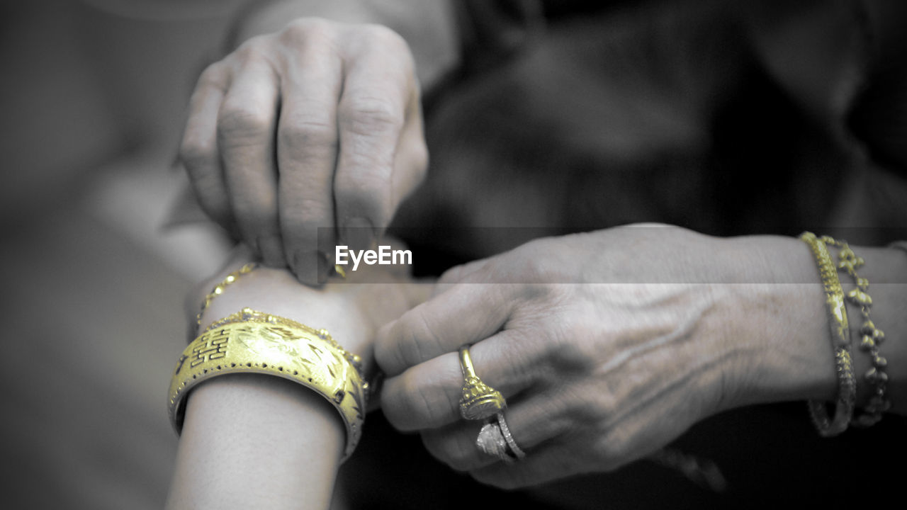 Cropped image of woman putting bracelet around brides hand
