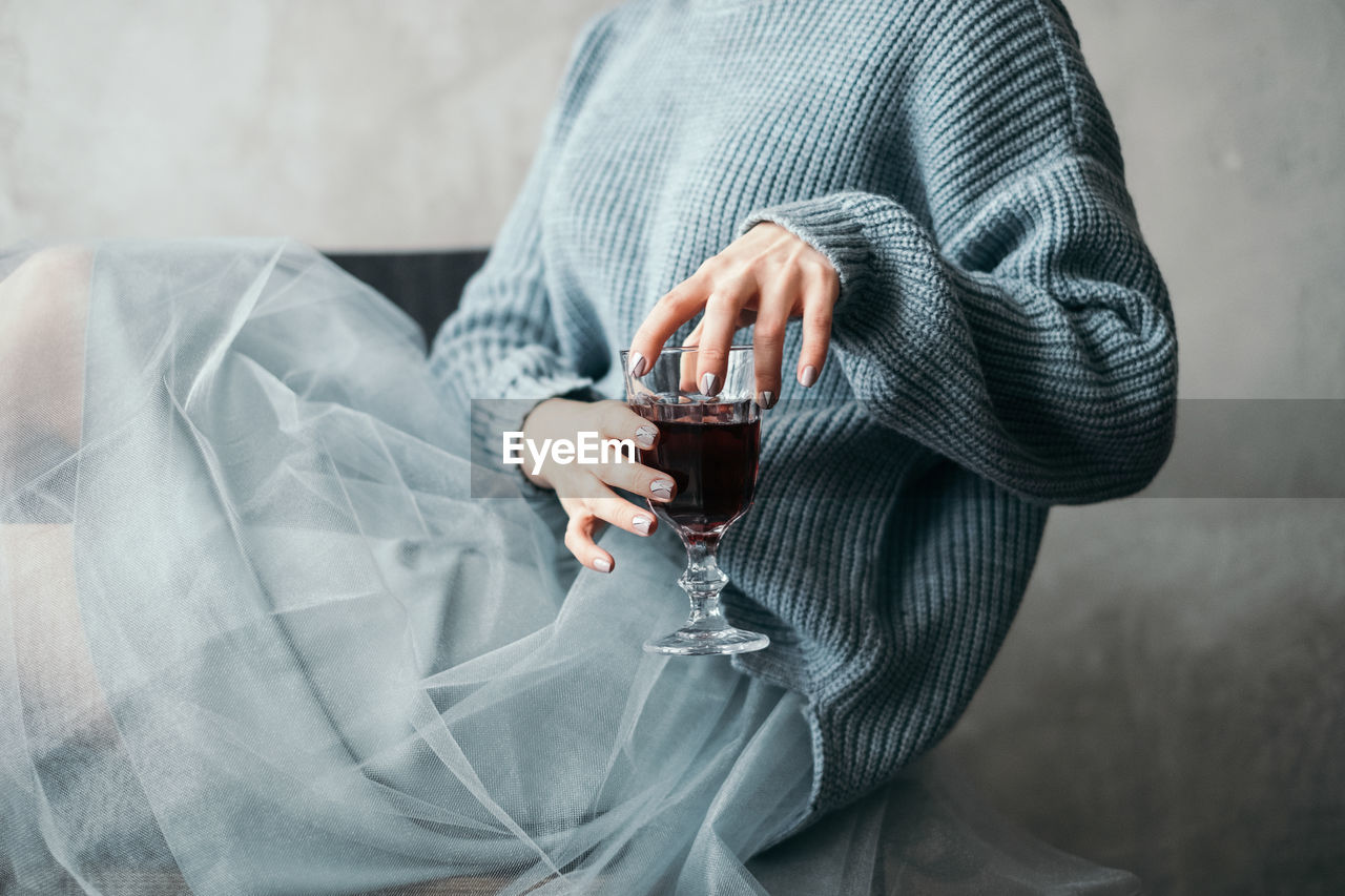 Midsection of woman having red wine at home