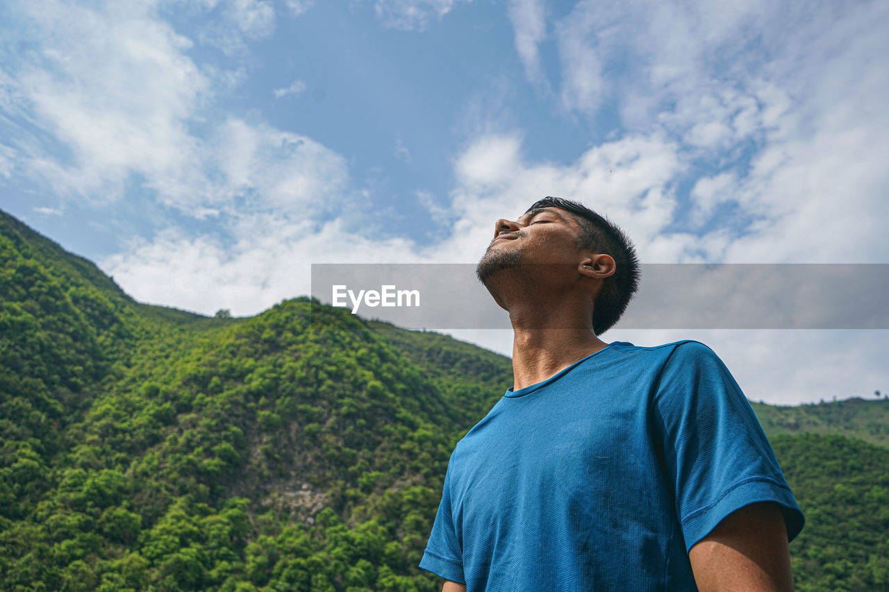 YOUNG MAN LOOKING AT MOUNTAINS AGAINST SKY