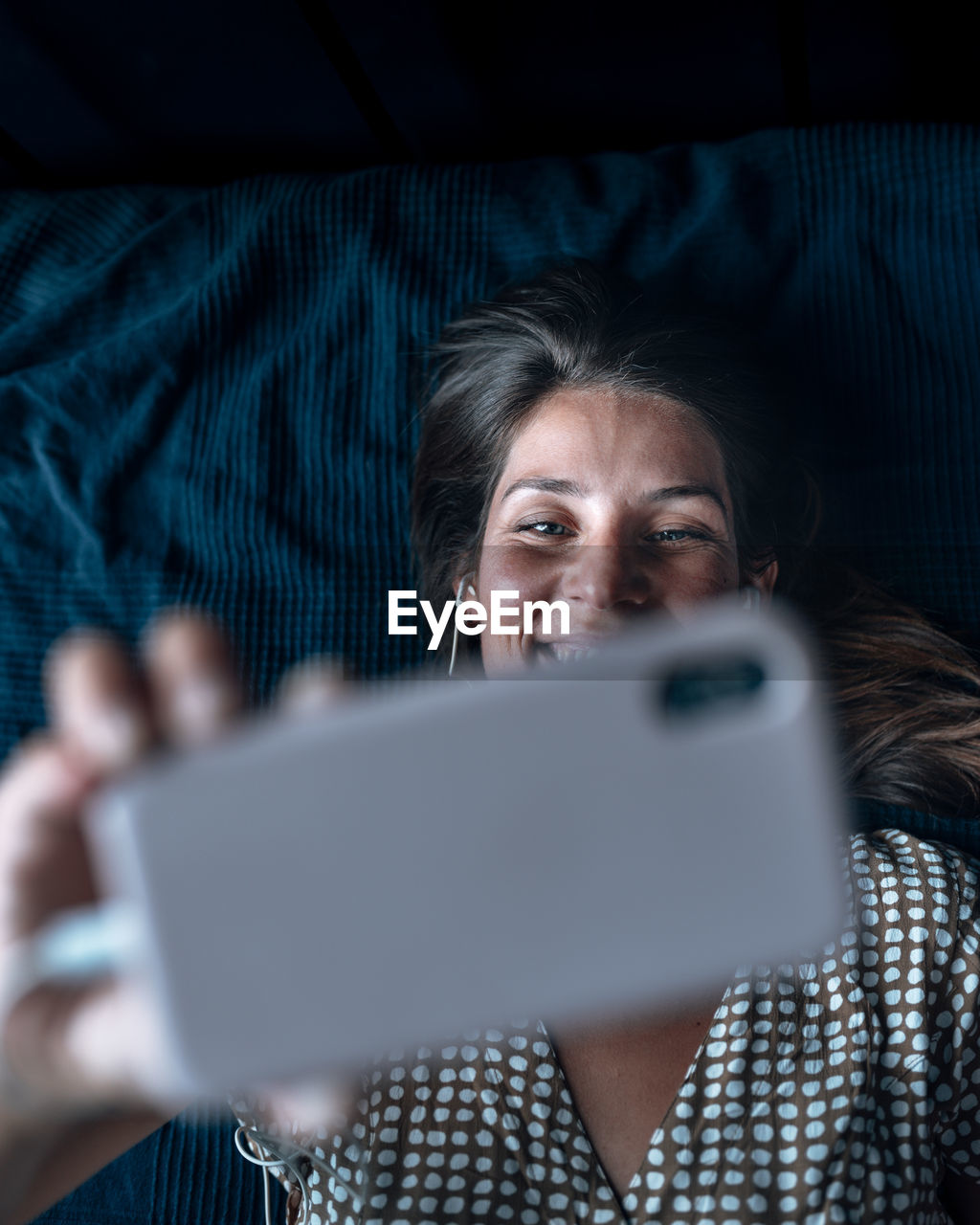 Directly above shot of woman on video call while lying in bed