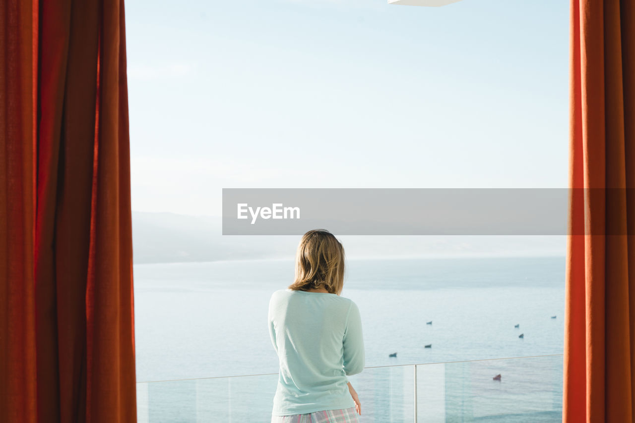 Woman looking at sea while standing in balcony against sky