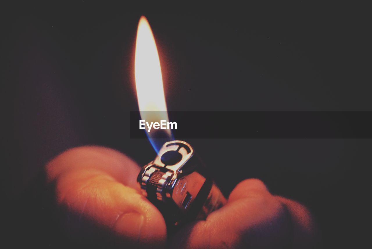 Close-up of hand holding lit cigarette lighter against black background