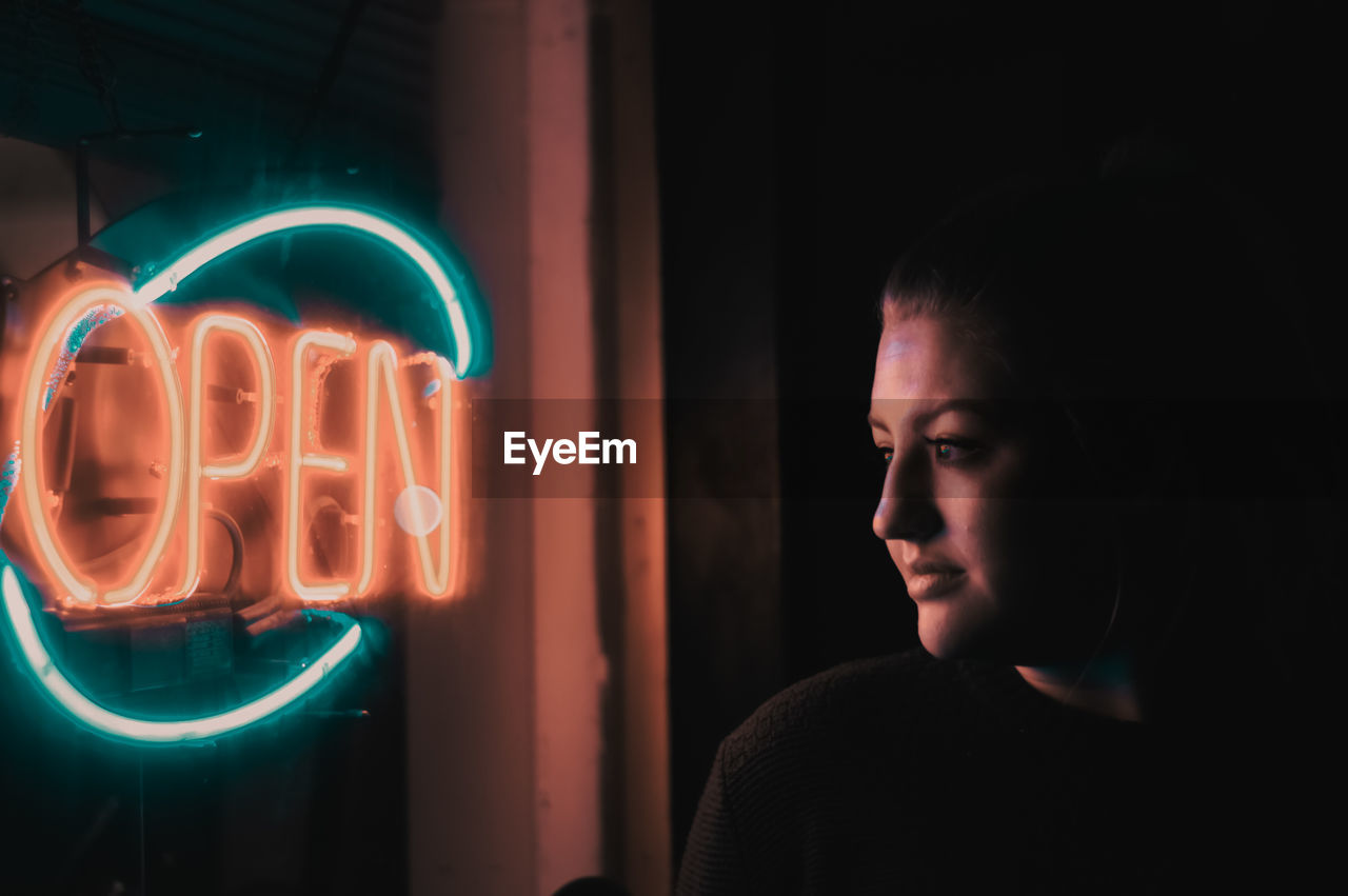 Close-up of woman looking at illuminated open store sign