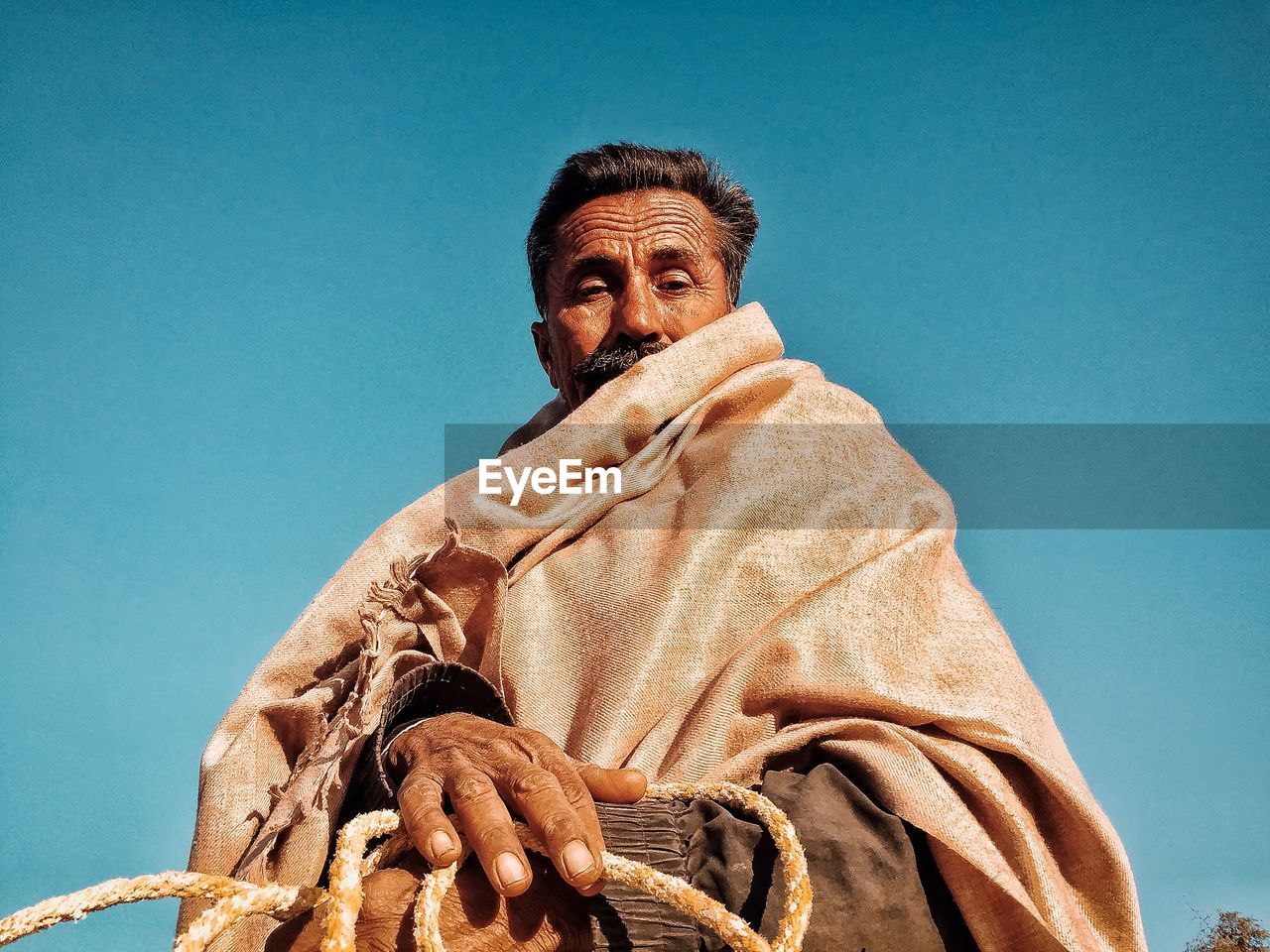 Low angle portrait of man wearing shawl against clear blue sky