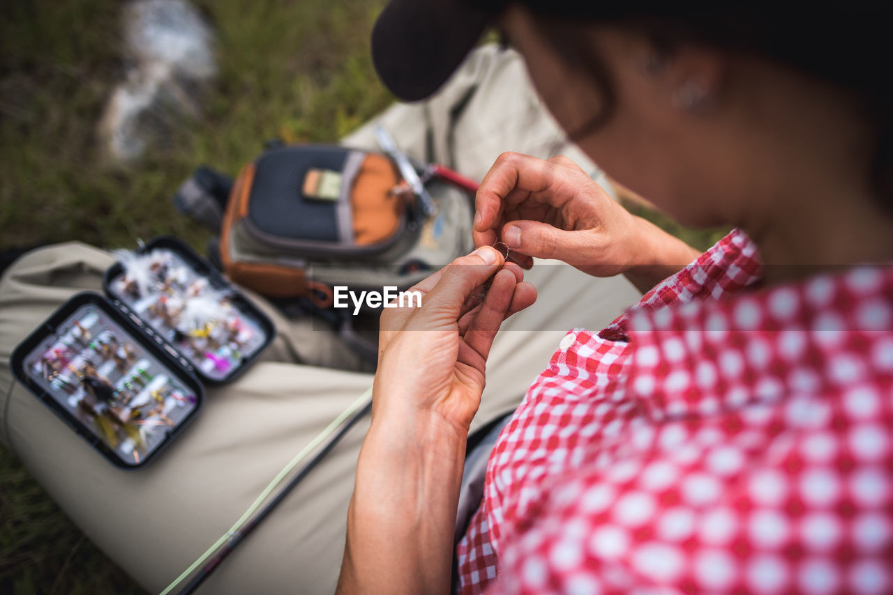 Woman angler ties fly onto end of fly fishing line while sitting