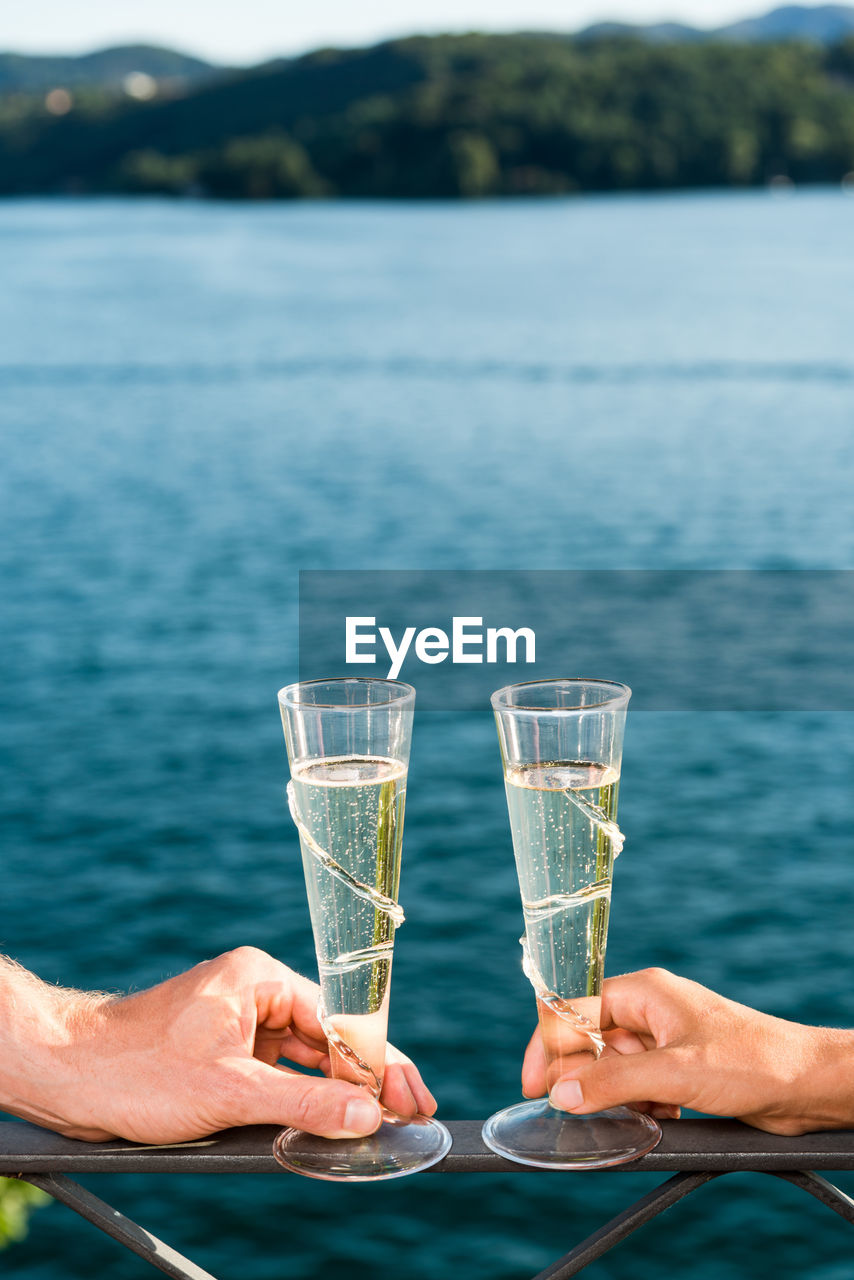 Close-up of couple hands holding champagne on railing by sea