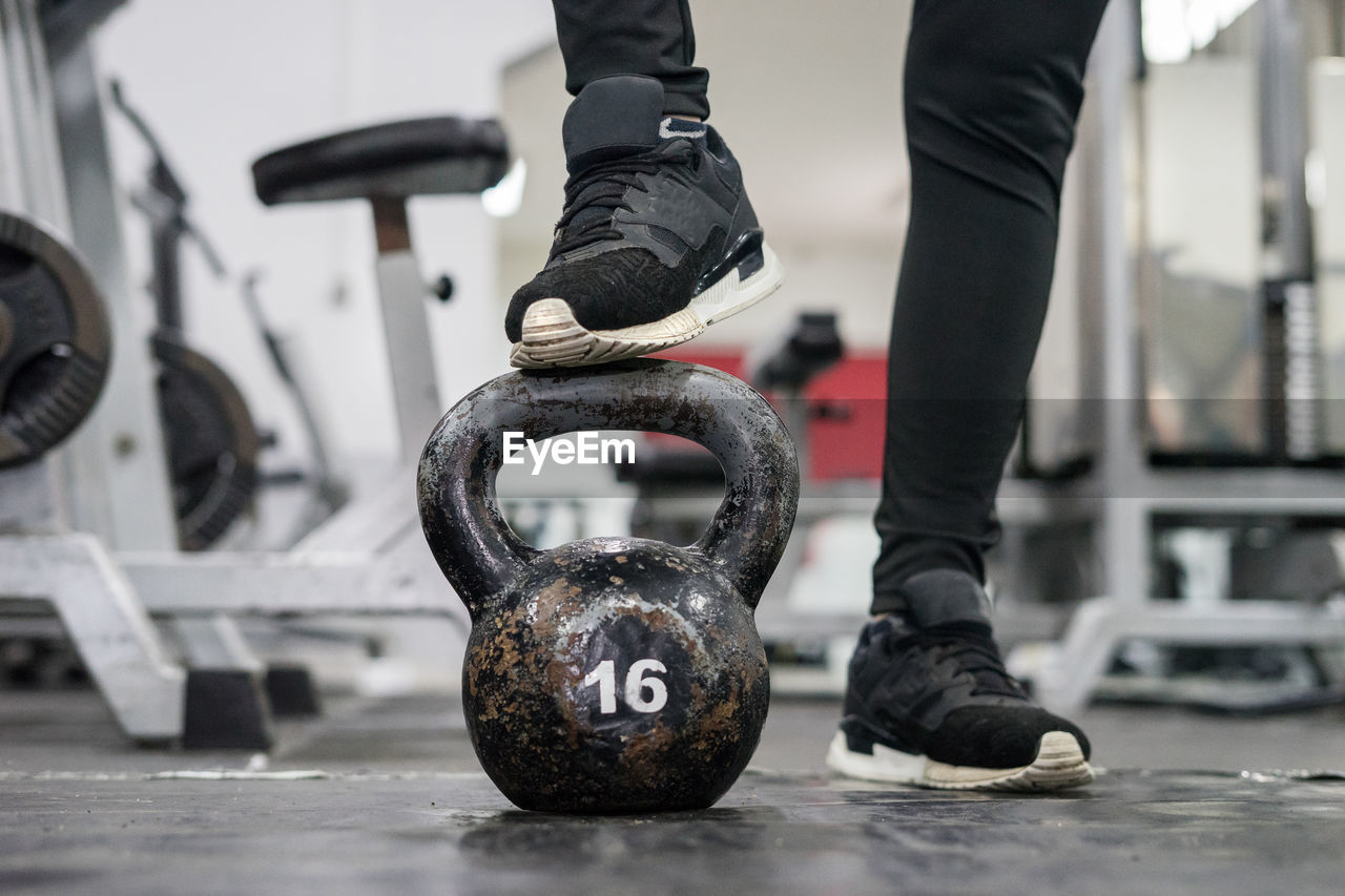 Low section of person standing on kettlebell at gym