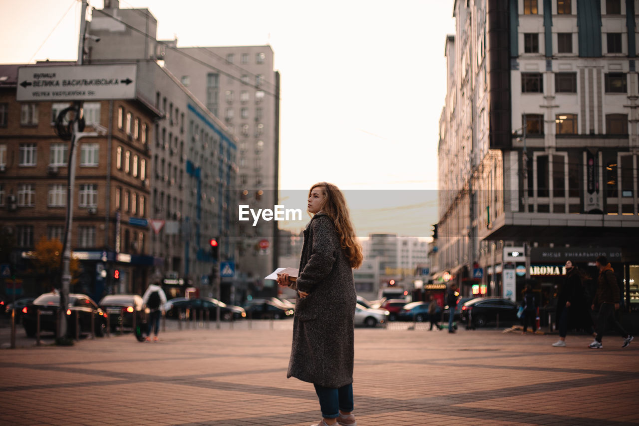 Thoughtful teenage student girl standing in city during autumn
