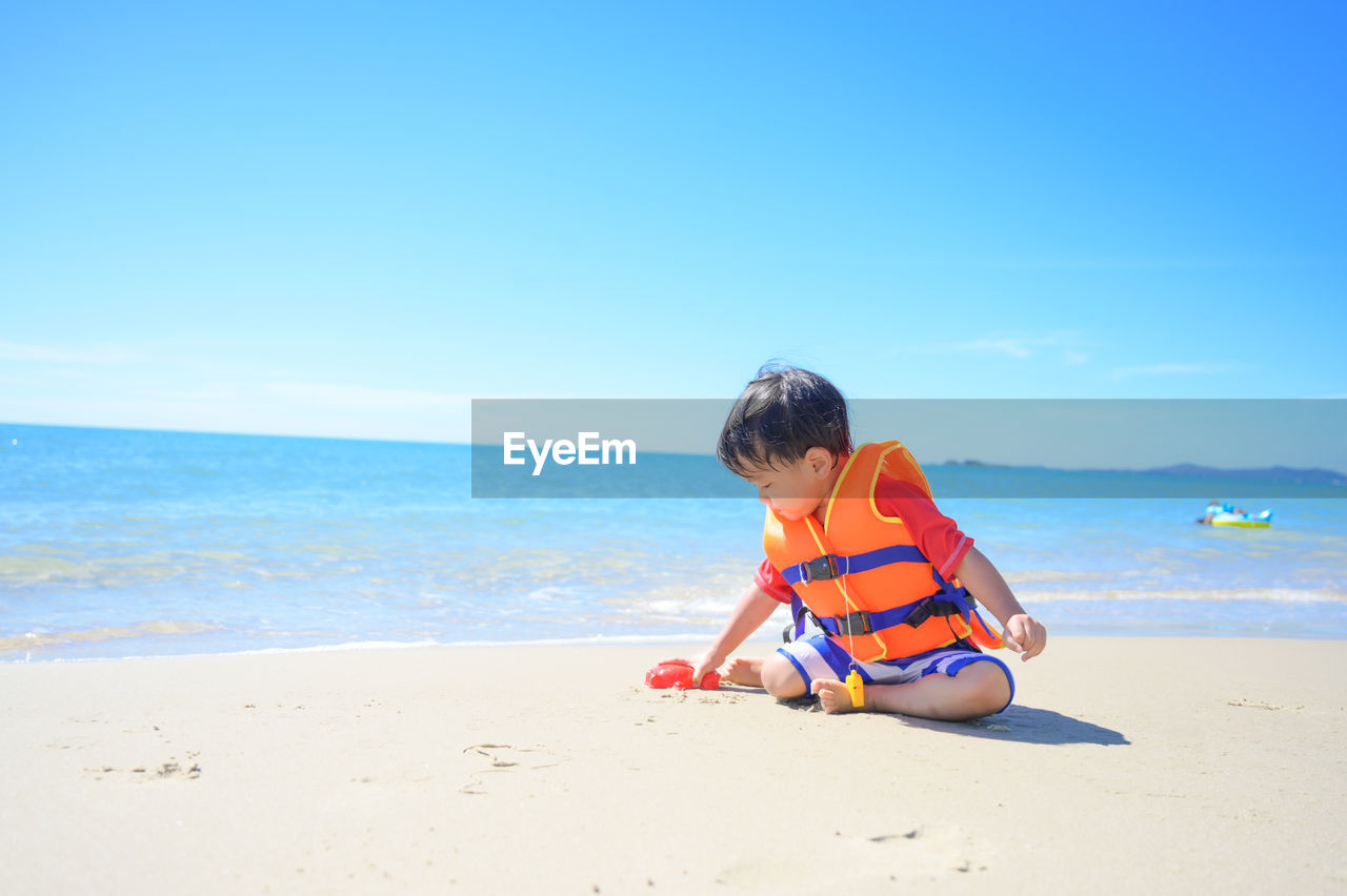 side view of boy playing on sand at beach against clear blue sky