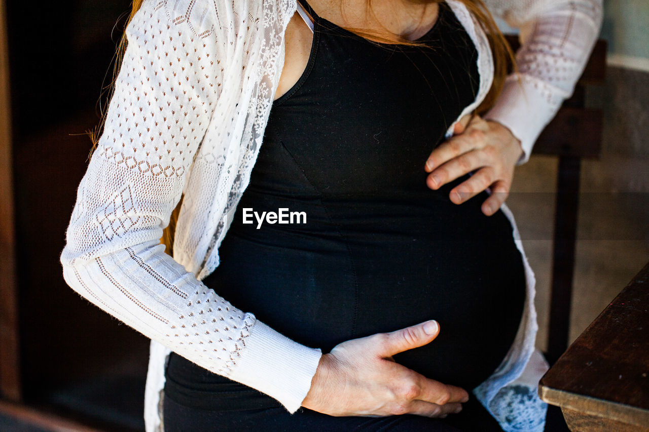 Midsection of pregnant woman holding belly at home
