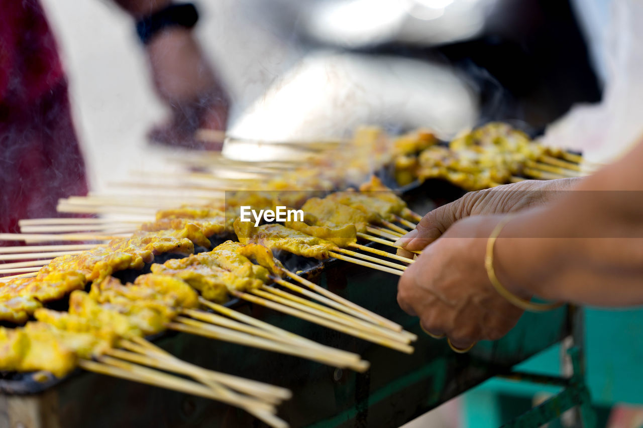 Cropped image of people roasted food in skewers on barbecue grill