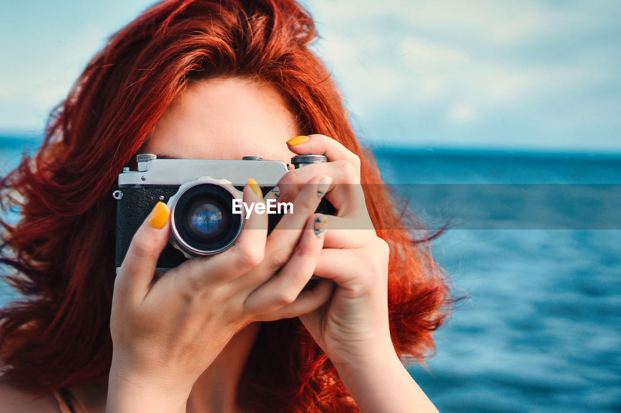 Red haired woman travel photographer, taking pictures on the background of the sea. 