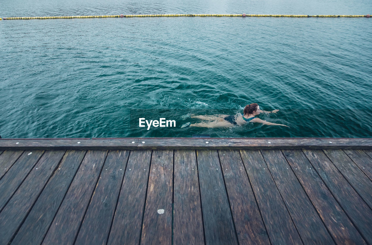 Woman swimming solo next to wooden dock in cold water in cdenmark