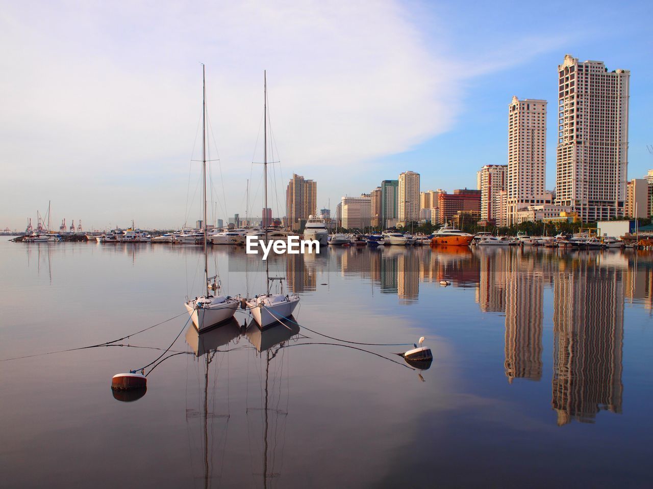 Sailboats moored in city by buildings against sky
