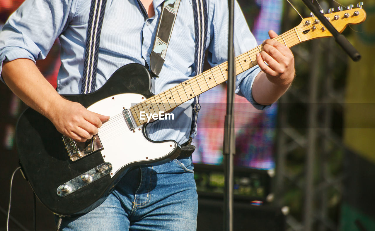 Midsection of man playing guitar at concert