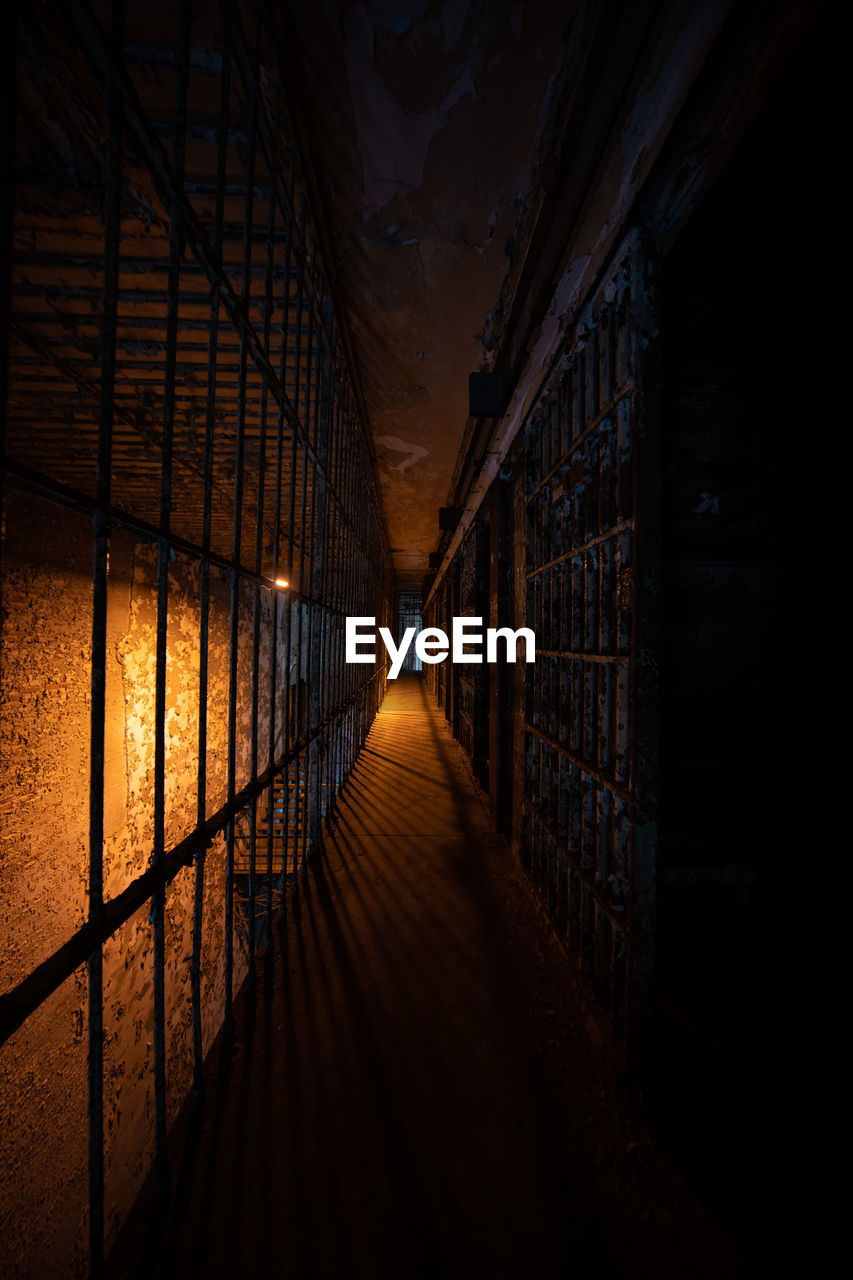 Dark hallway of prison bars in front of cells in an unknown prison cell block
