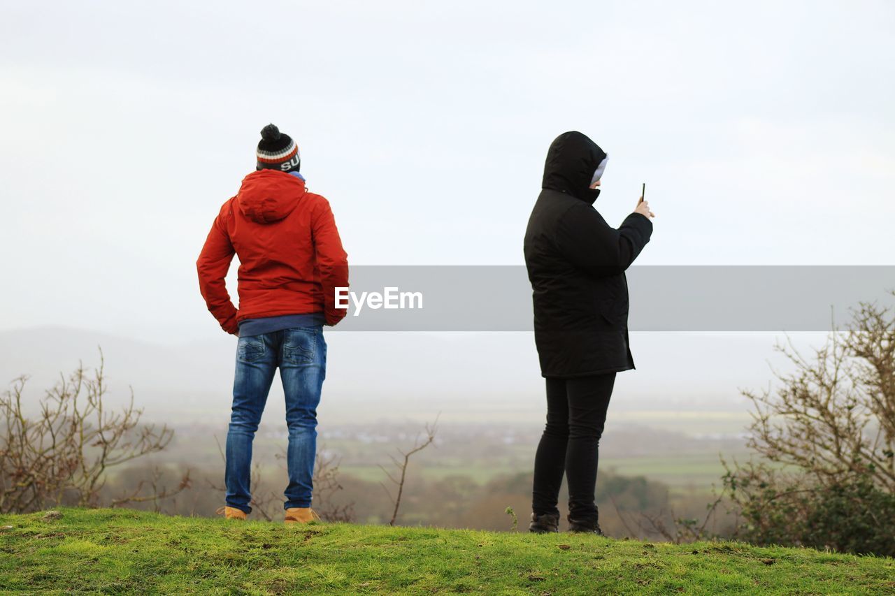 People standing on grassy field against sky during foggy weather