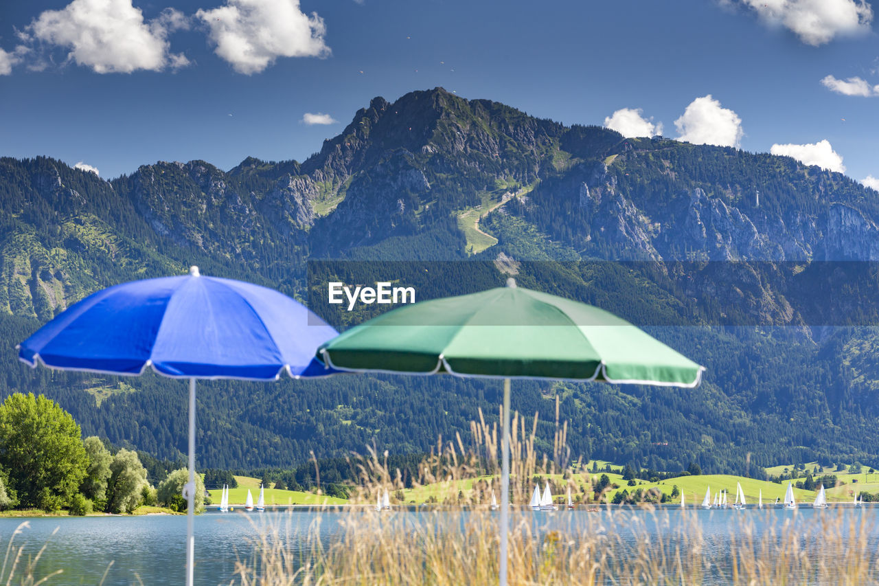 Parasols by forggensee lake against tegelberg mountain