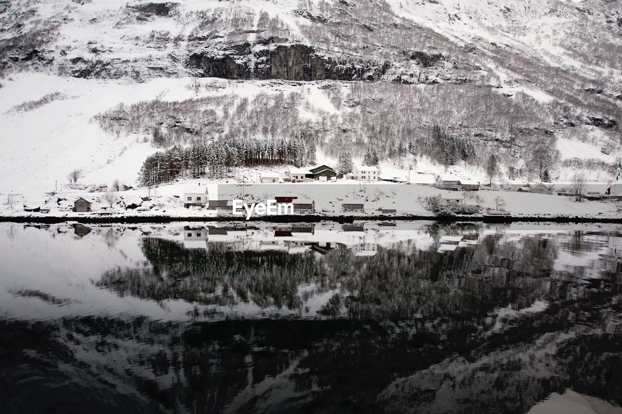 Snowcapped houses against mountain with reflection in lake