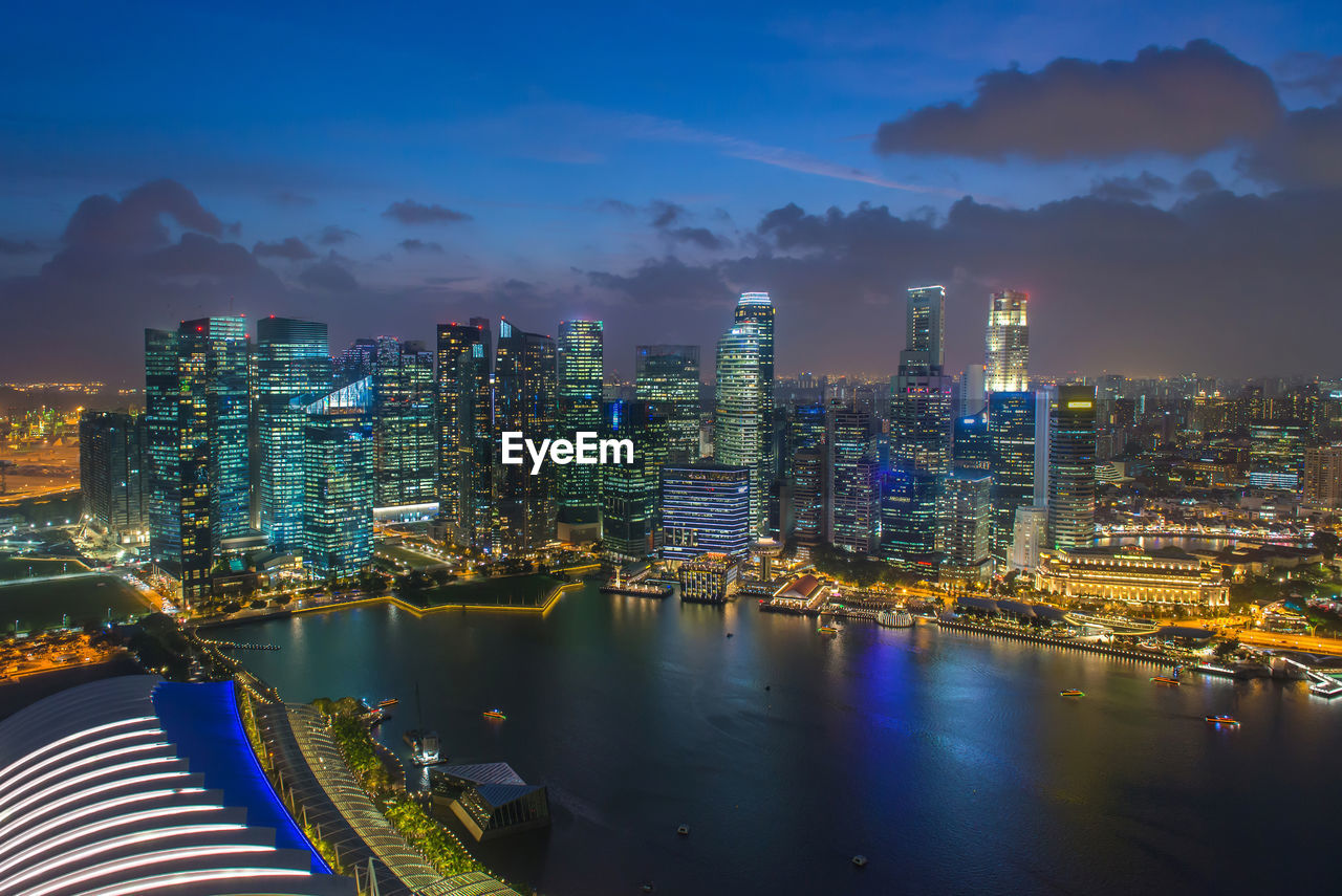 Illuminated city by river against sky at night