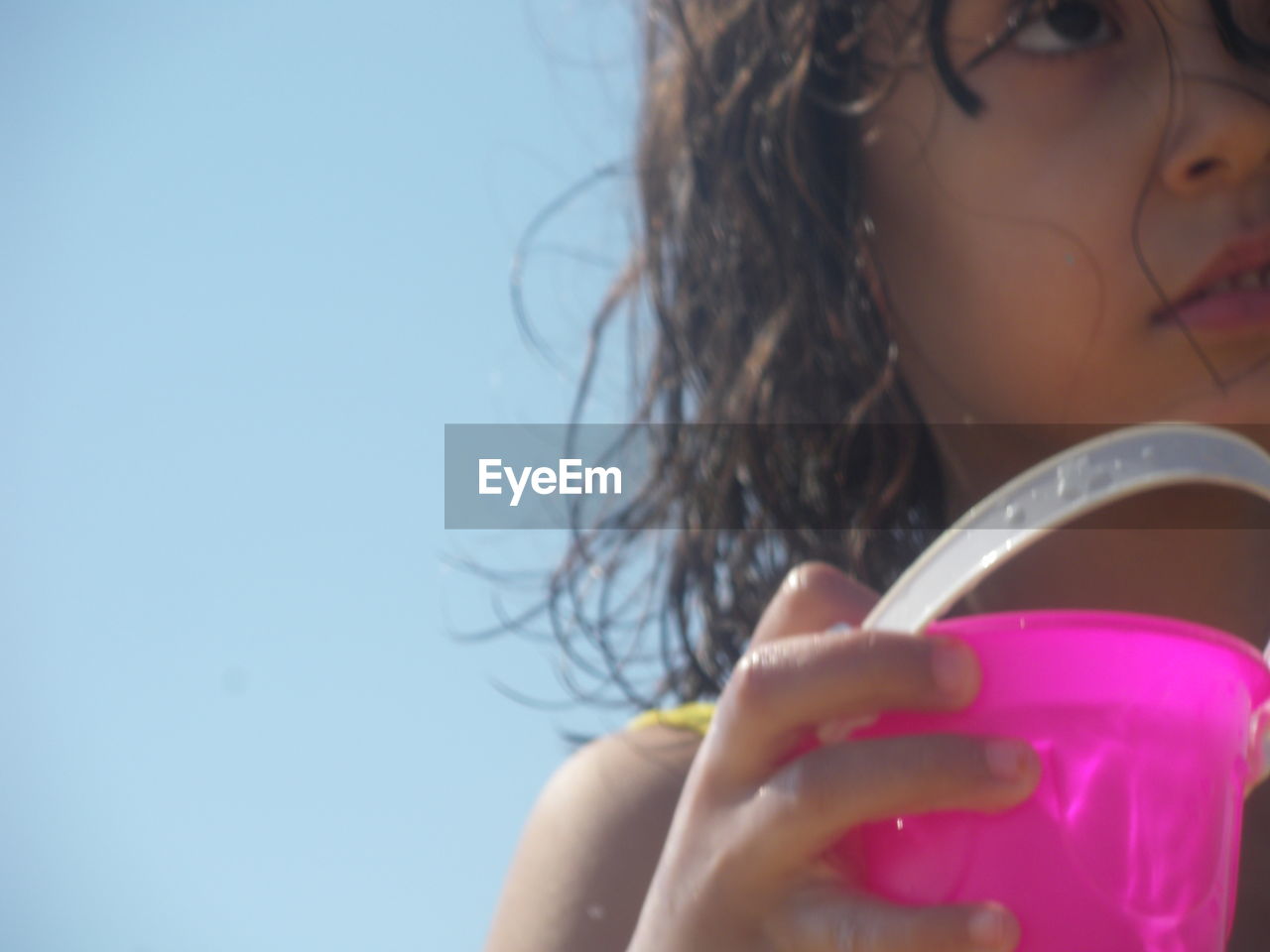 Close-up of girl holding plastic bucket against clear sky