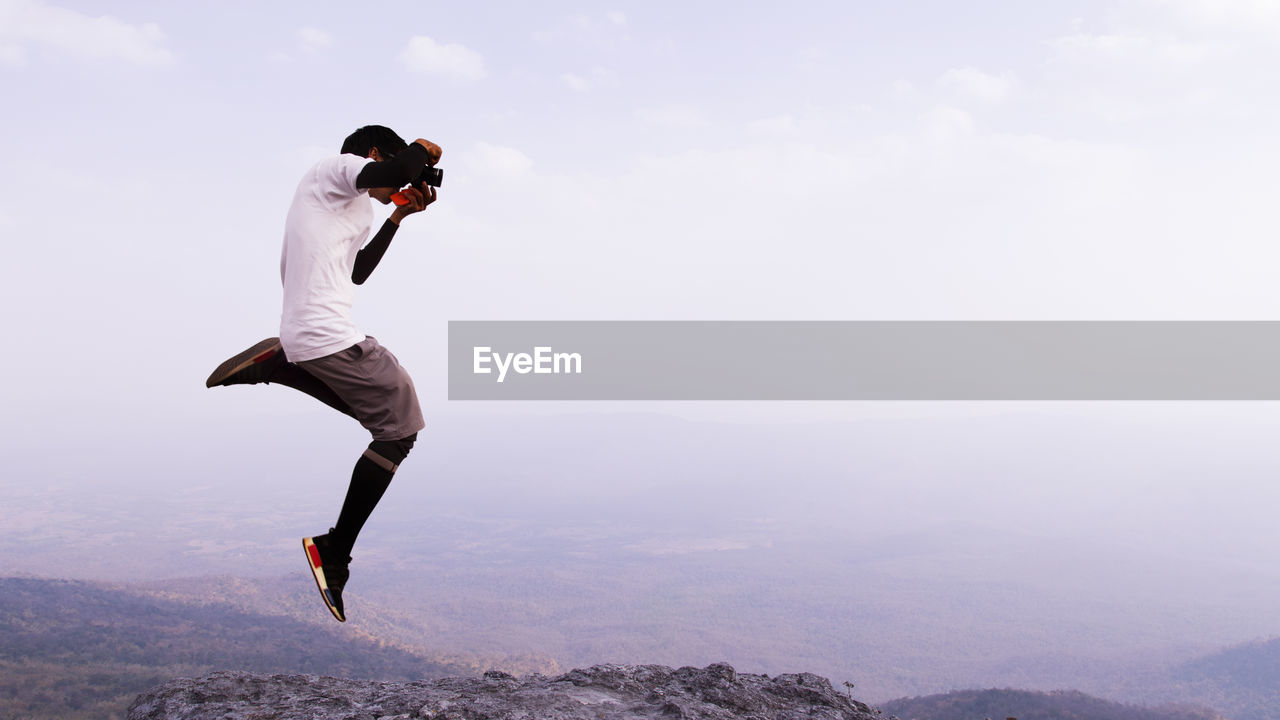 Man photographing while jumping against sky