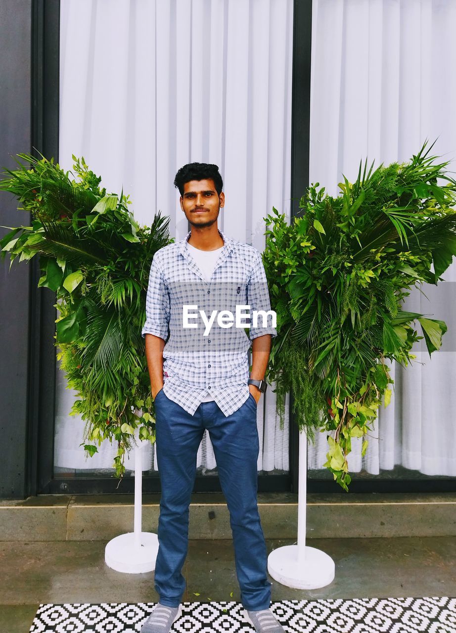 Full length portrait of young man standing in potted plant