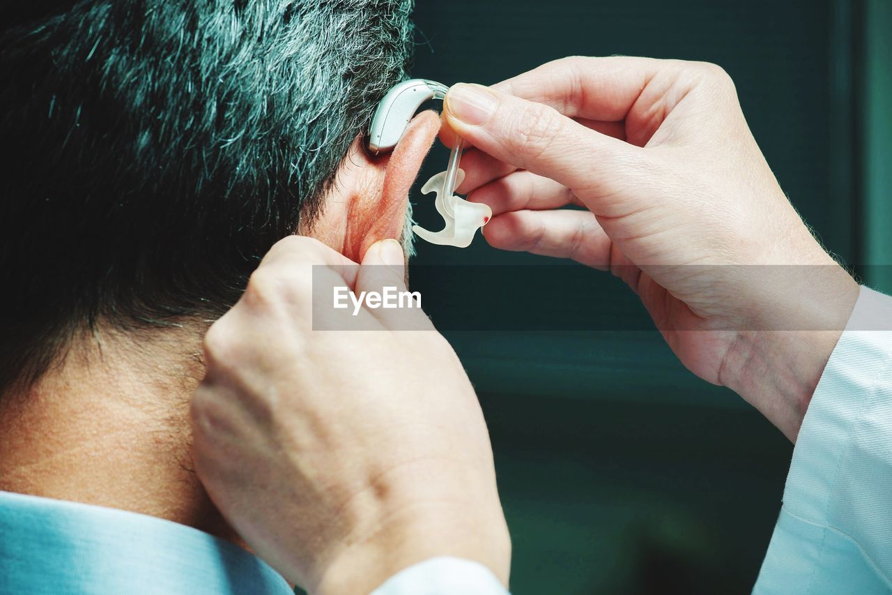 Cropped hand of person adjusting man hearing aid