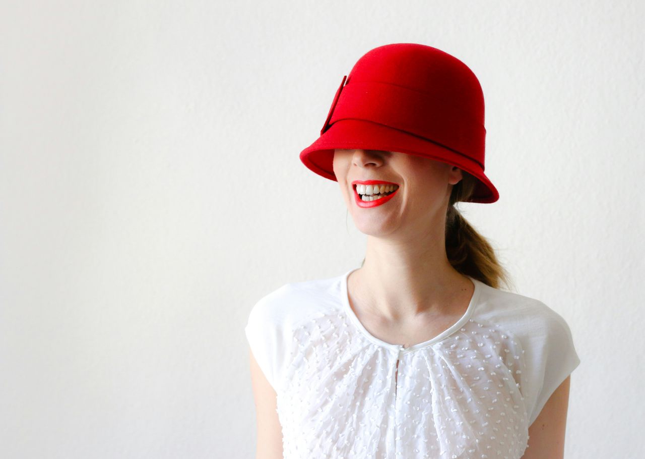 Portrait of smiling young woman wearing red hat against white background