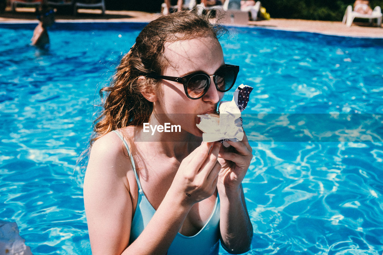 Woman in sunglasses eating food at swimming pool