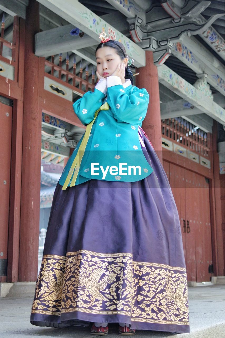 Low angle view of young woman wearing costume standing against built structure