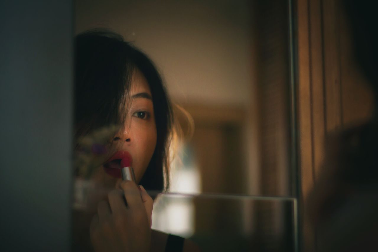 Reflection of woman applying lipstick on mirror at home