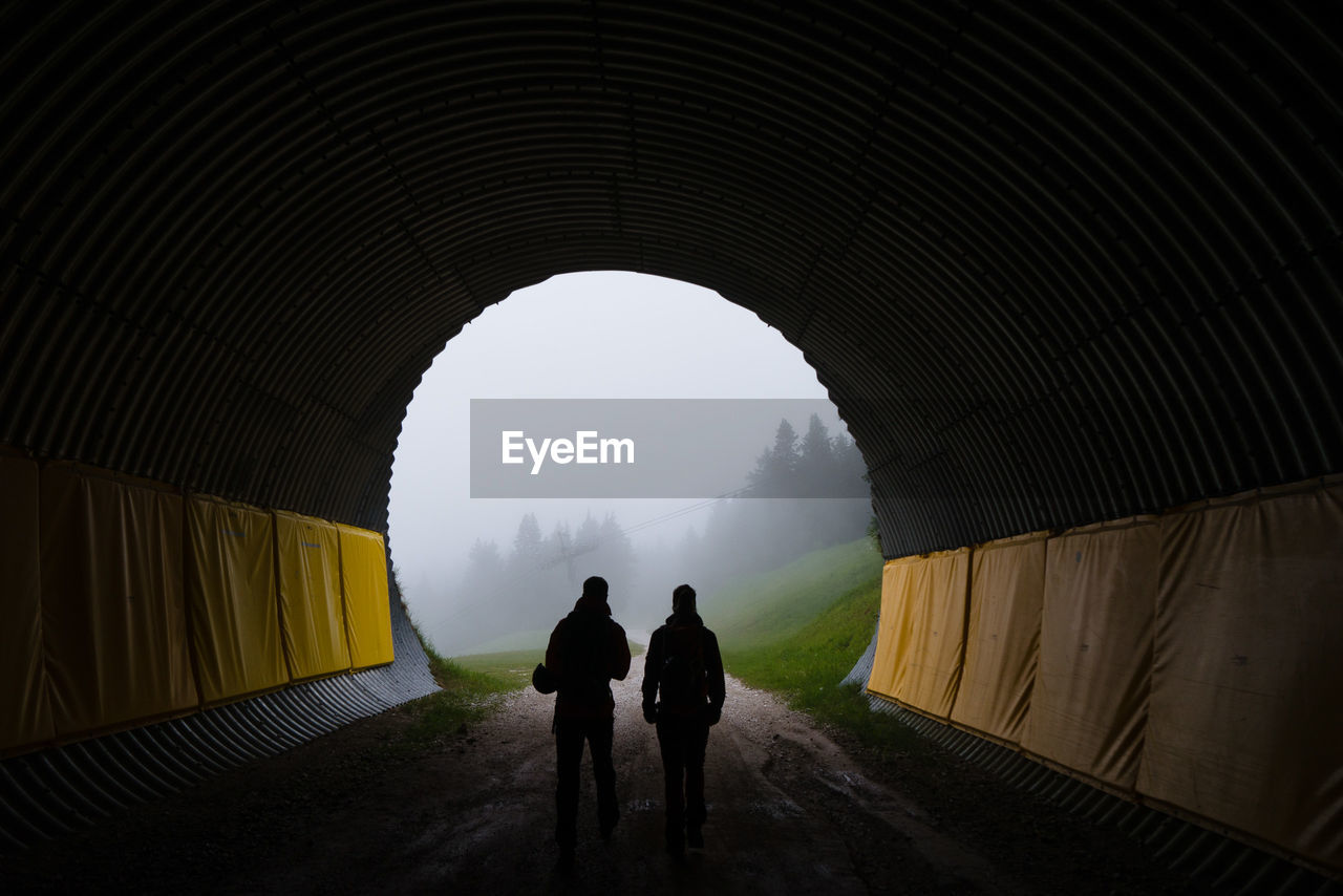 Rear view of silhouette people walking in tunnel during foggy weather