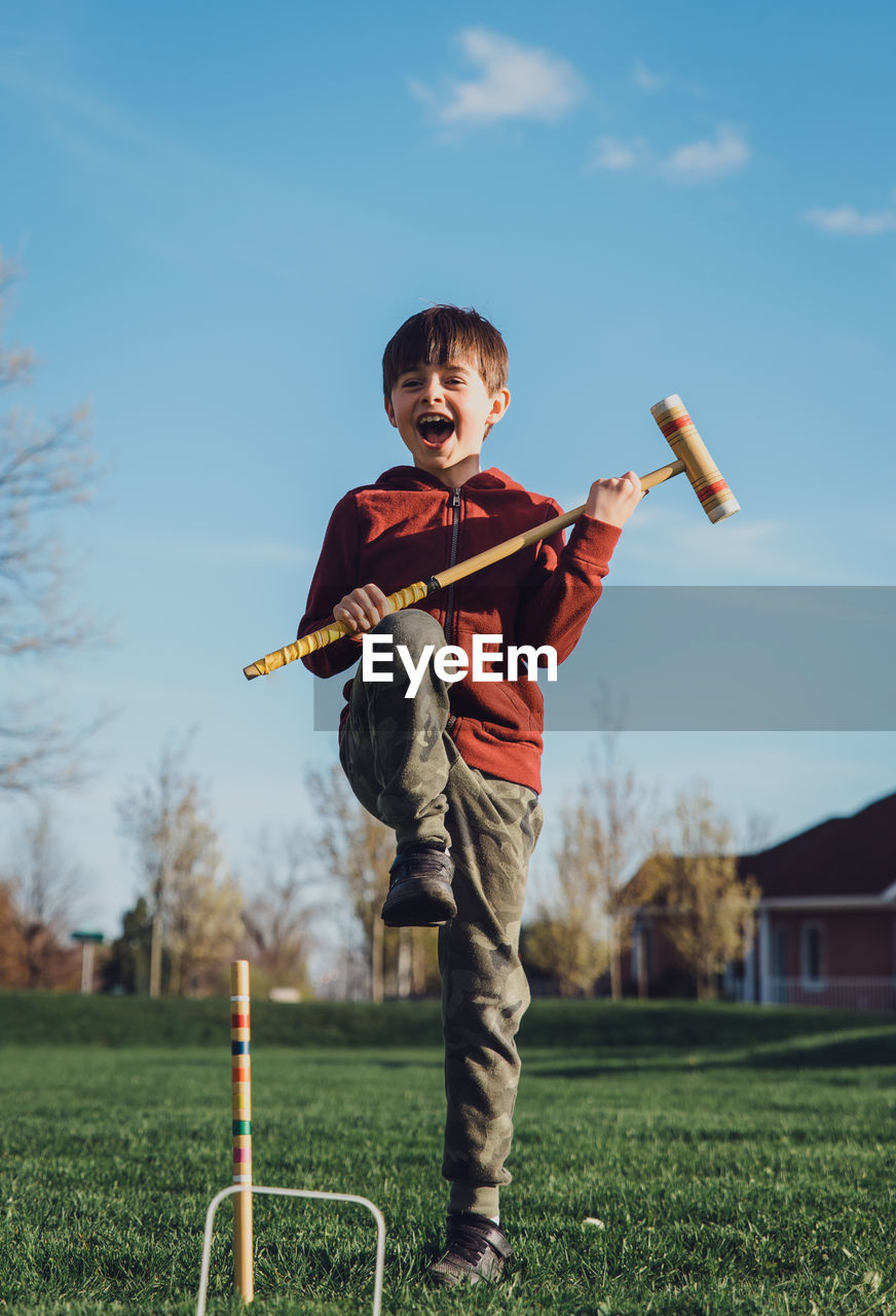 Young boy doing an excited jump while playing croquet outside.
