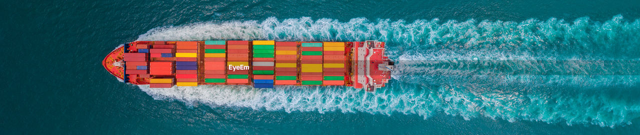 Aerial top view of cargo ship with contrail in the ocean sea ship carrying container and running 