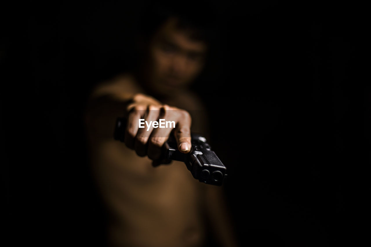 Shirtless man aiming gun against black background