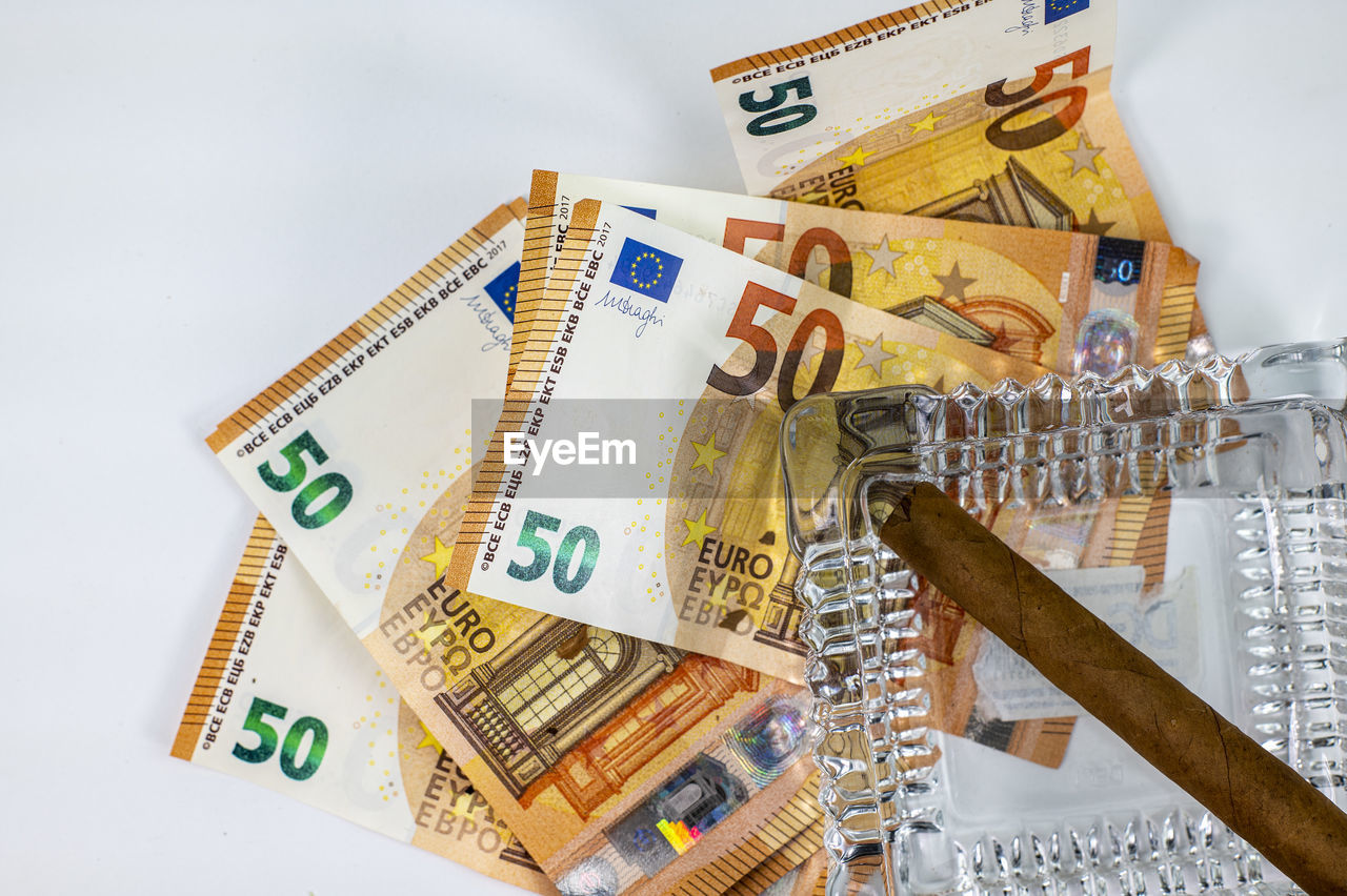 Close-up of banknotes with cigar over white background