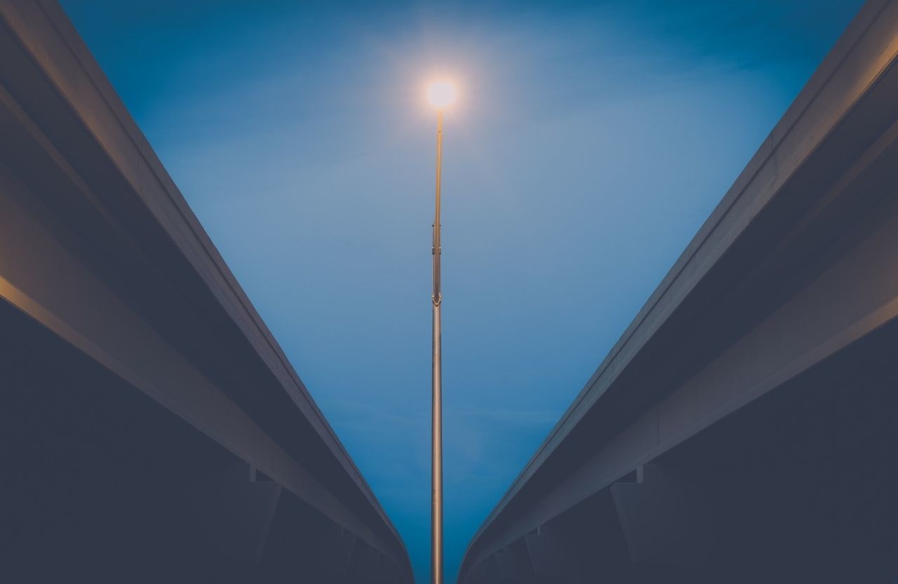 Low angle view of cropped bridges and lit street light against blue sky