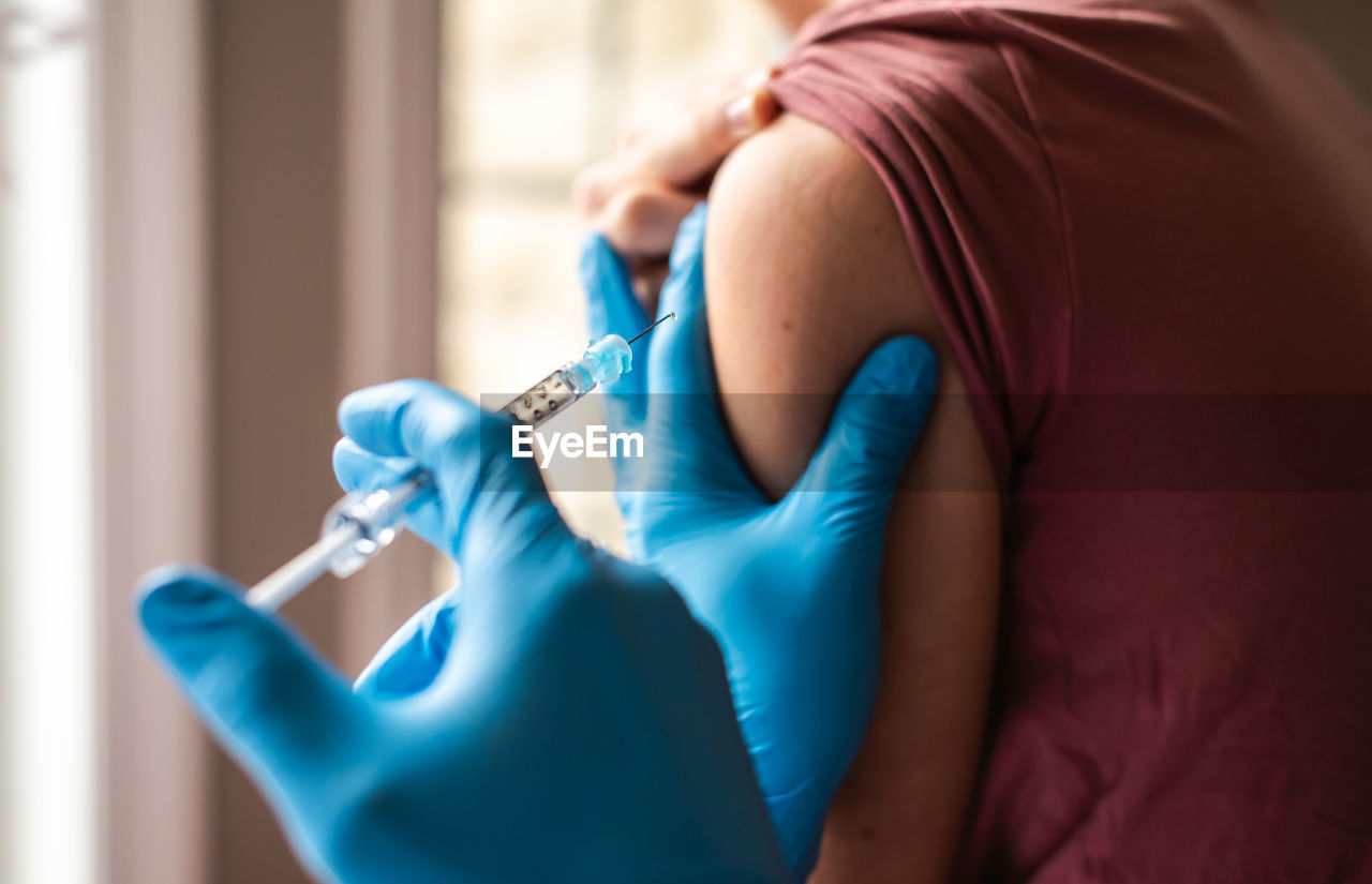 Close up of teen boy getting vaccinated by doctor holding a needle.