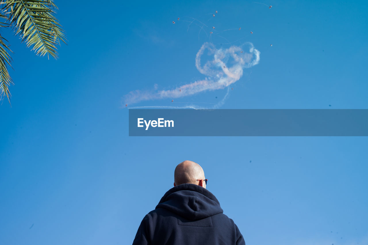 Low angle view of man against vapor trail in sky on sunny day