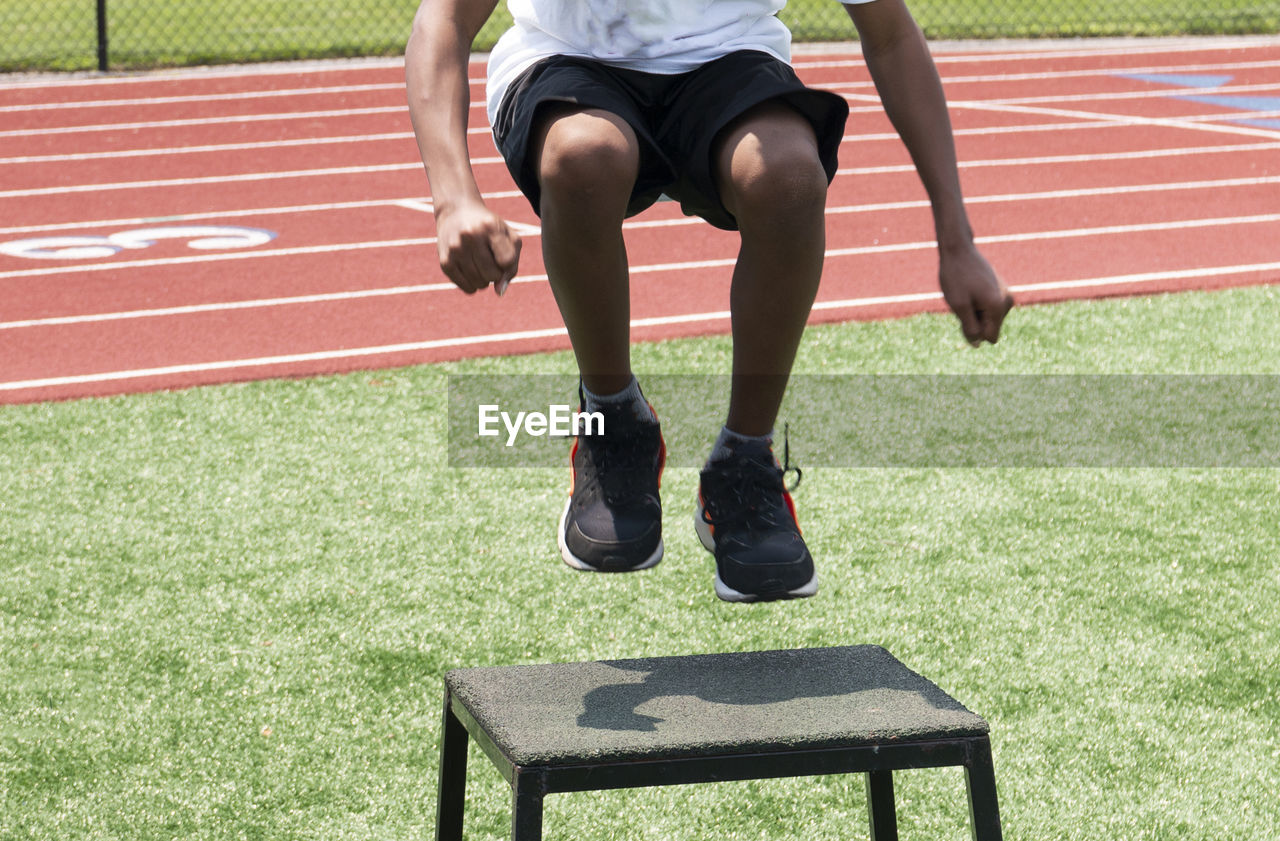 Front view of a young athlete jumping onto a plyo box during a high school summer sports camp.