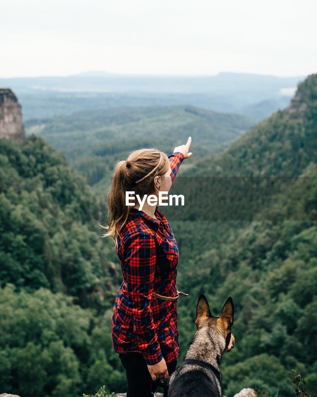 Side view of woman pointing while standing with dog against mountains