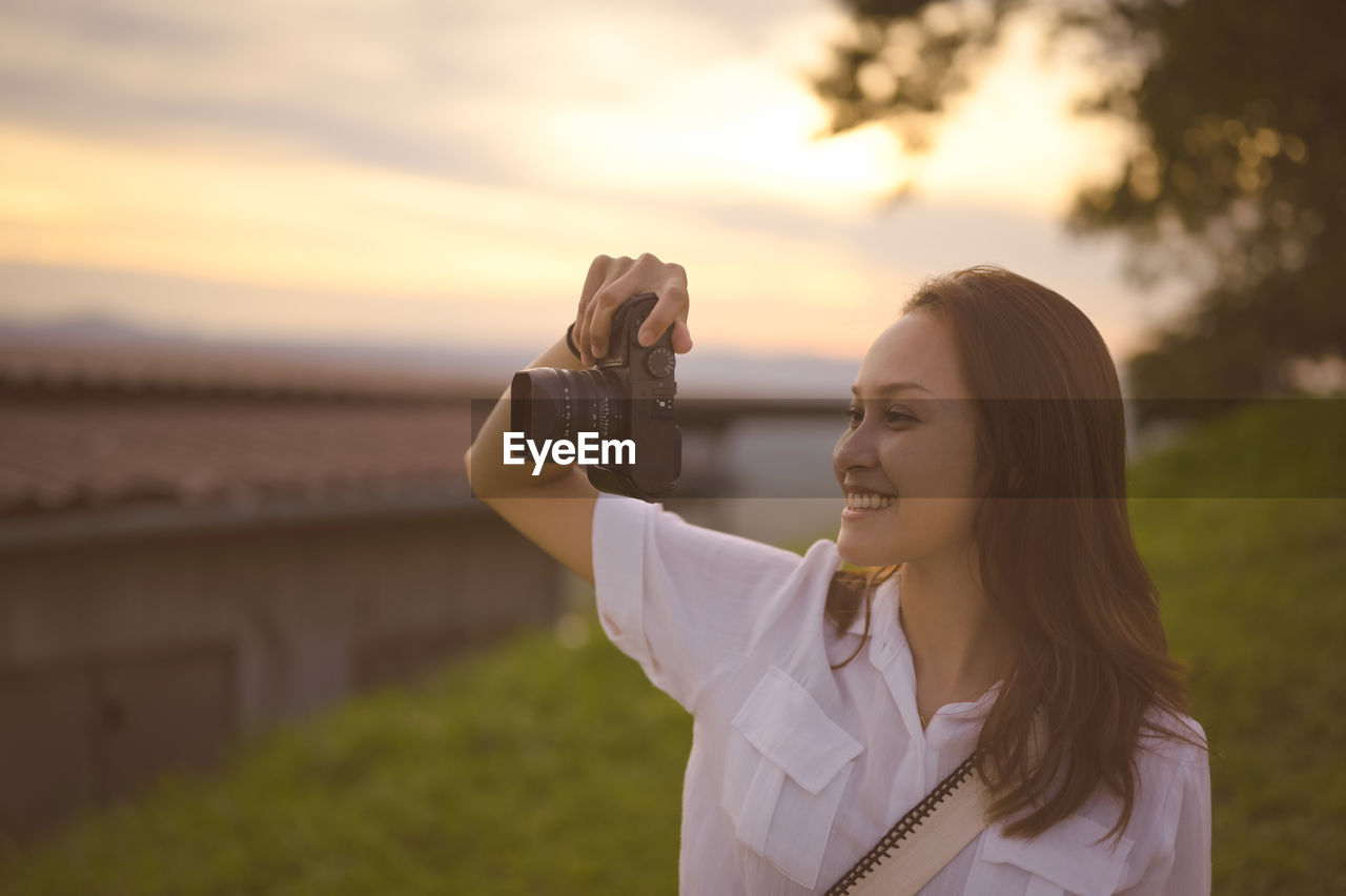 Happy young woman enjoy using camera in golden hour
