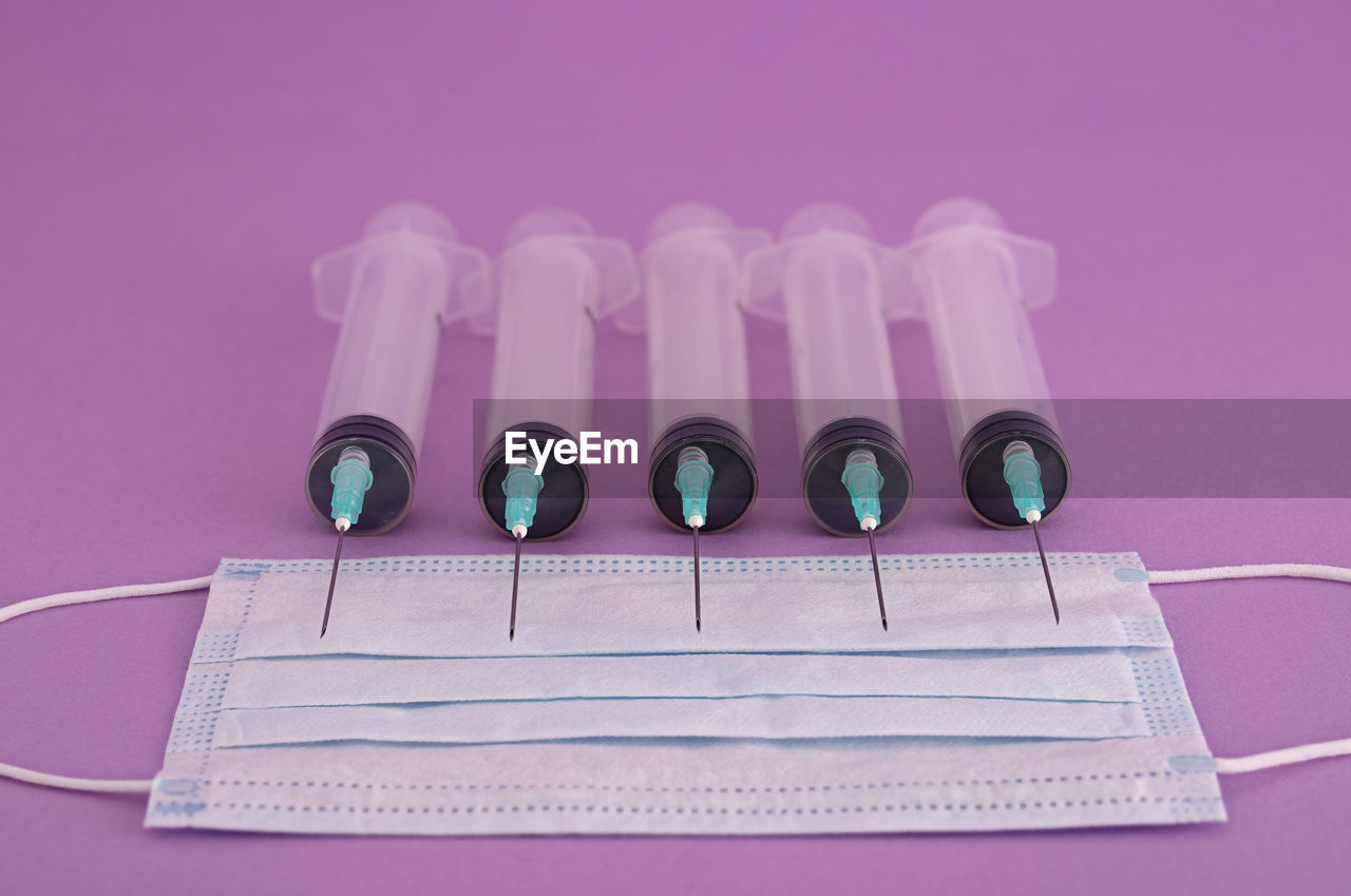 Close-up of syringes and mask on pink background